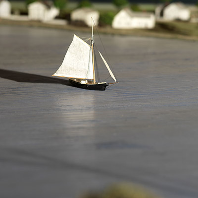 A small sailboat with white sails sails on calm waters near a shoreline with several houses in the background.