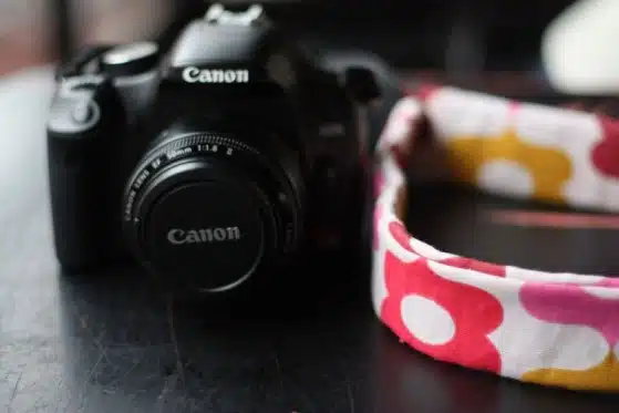 A Canon DSLR camera sits on a surface next to a multicolored floral-patterned strap.