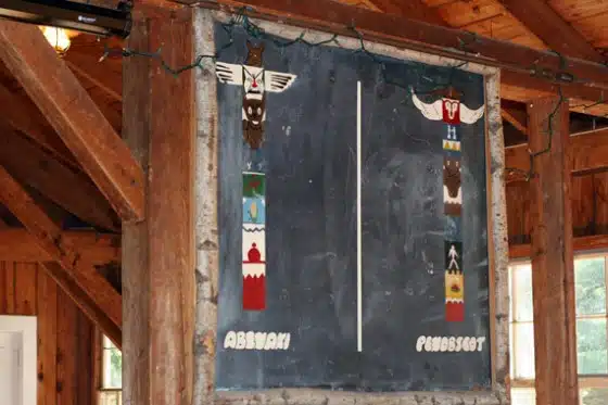 A chalkboard mounted on a wooden frame displays two totem pole designs labeled "Abnaki" and "Penobscot," each with colorful segmented designs.