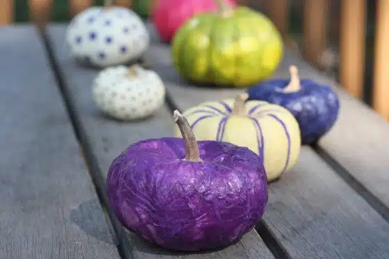 Colorful painted pumpkins in various shades and patterns are displayed on a wooden surface outdoors.