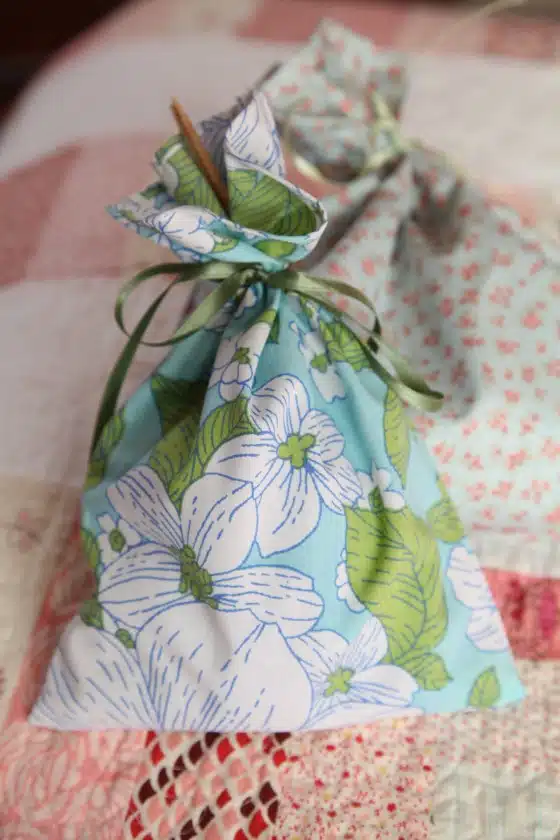 A small fabric bag with a floral pattern and tied with a green ribbon is placed on a quilted surface.