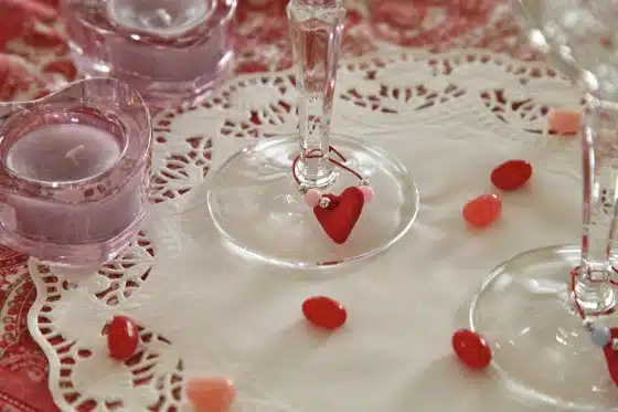 A close-up of a decorated table with candle holders, a doily, wine glasses with heart-shaped charms, and colorful jelly beans scattered around.