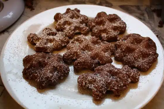 A plate of six chocolate cookies shaped like snowflakes, dusted with powdered sugar.