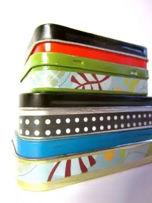 A stack of six rectangular, decorative tin boxes in different colors and patterns, arranged one on top of another against a white background.