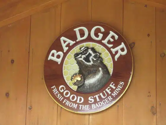 Round wooden sign with a badger holding a honeycomb that reads, "BADGER GOOD STUFF FRESH FROM THE BADGER MINES." Mounted on wooden wall.