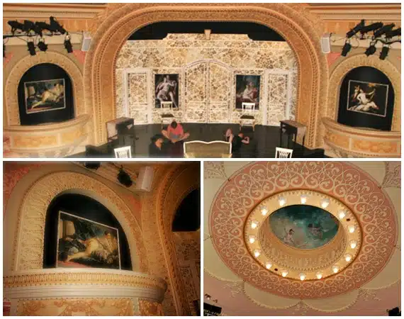 Interior of a lavishly decorated theater featuring a stage with ornate backdrops, decorative wall art, and an elaborately designed ceiling with a circular chandelier.