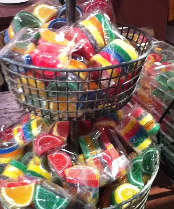 A tiered metal basket holds numerous packets of colorful, assorted fruit-shaped jelly candies wrapped in clear plastic bags.