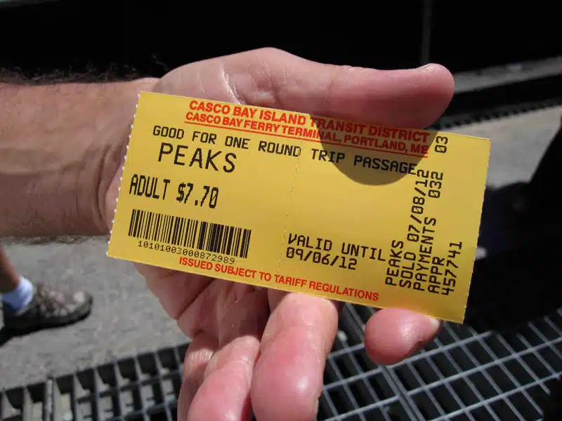A hand holding a yellow round trip ticket for Peaks Island from Casco Bay Island Transit District in Portland, ME, costing $7.70 for an adult and valid until September 6, 2012.