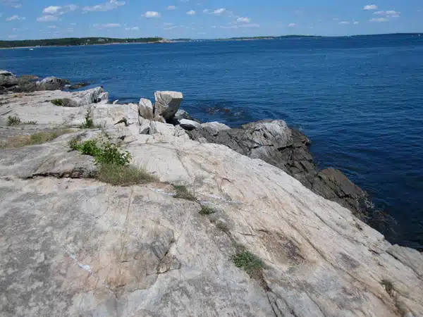 Rocky coastline with large rock formations extending into a blue ocean under a partly cloudy sky.