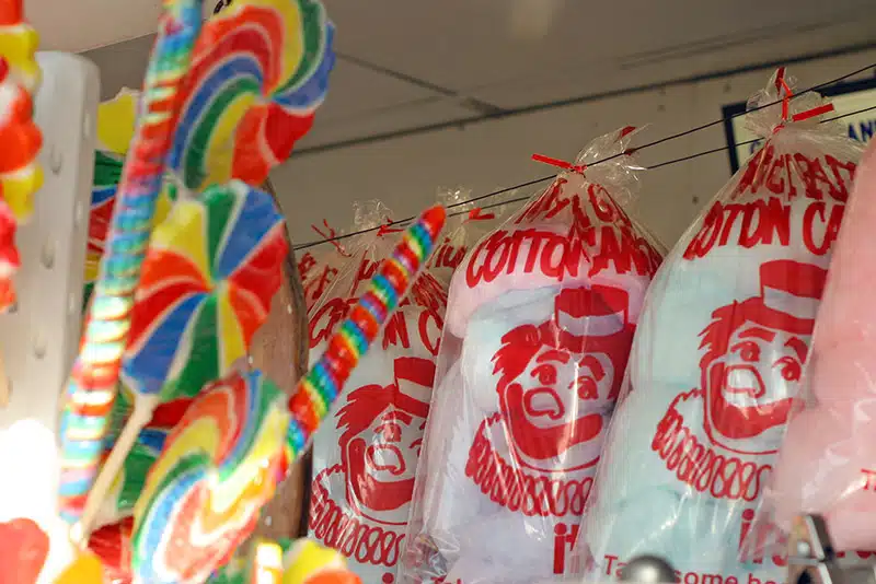 Bags of multicolored cotton candy hang on a display, with rainbow swirl lollipops visible in the foreground.