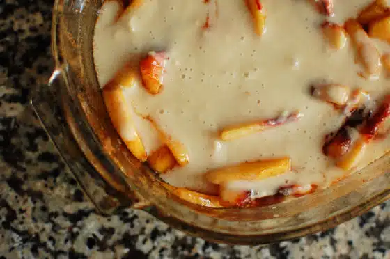 A glass dish filled with a creamy mixture and pieces of fruit, placed on a speckled countertop.