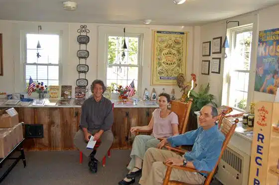 Three people sitting in a cozy room with various framed items and decorations on the walls, including American flags and a yellow vintage poster.