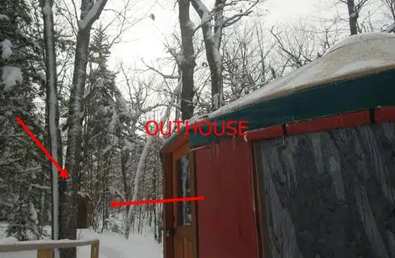 A snow-covered outdoor scene with trees and a partially visible structure. Red arrows point to an outhouse in the background labeled "OUTHOUSE.