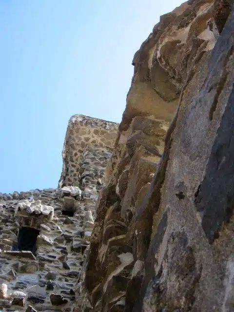 Close-up view of a stone structure with a clear blue sky in the background, showcasing architectural details and textures of the stonework.