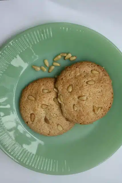 Two cookies with nuts on a green plate, with a few extra nuts beside the cookies. Gluten-Free Macaroons.