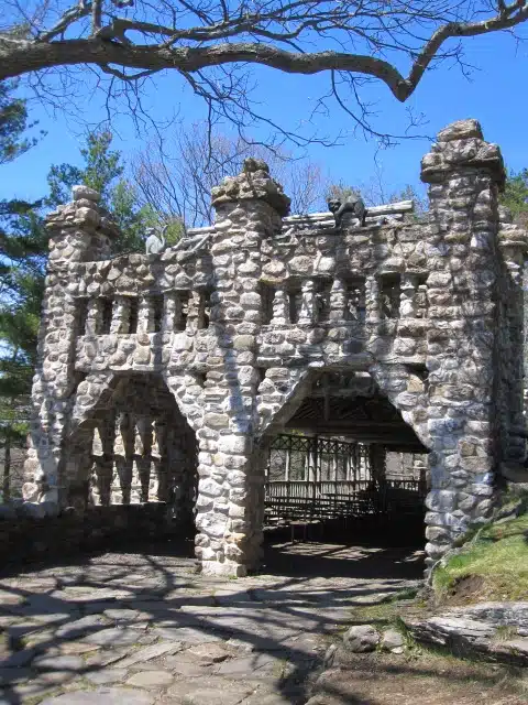 An old stone structure with two archways and a flat top, surrounded by trees and a blue sky.