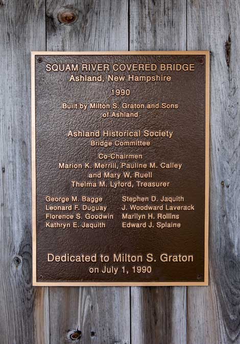 Bronze plaque on wood commemorating the Squam River Covered Bridge built in 1990 by Milton S. Graton and Sons. The plaque details Ashland Historical Society and dedication to Milton S. Graton on July 1, 1990.