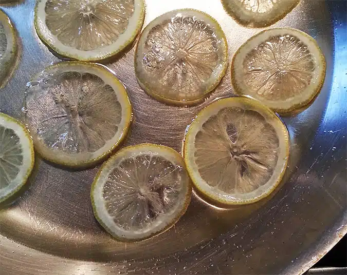 Slices of lemon in a shiny metal pan with some liquid.