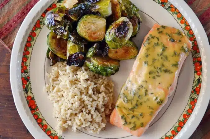 A plate with baked salmon topped with herb sauce, roasted Brussels sprouts, and a serving of rice.