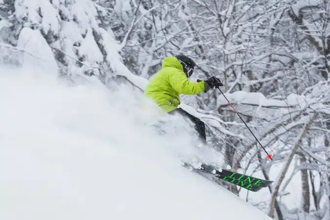 A skier in a bright green jacket glides down a snowy slope, surrounded by snow-covered trees.