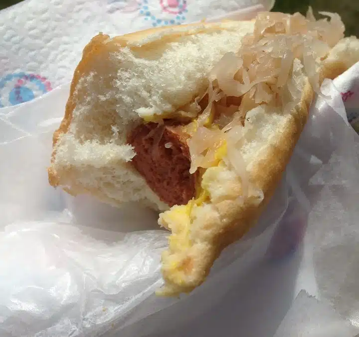 A bitten hot dog in a bun with sauerkraut and mustard, placed on a white napkin.