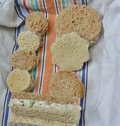 Various shapes of bread slices and a sandwich piece with filling are arranged on a colorful striped cloth.