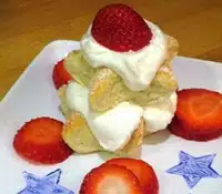 A dessert consisting of layers of ladyfingers, whipped cream, and fresh strawberries on a white plate, garnished with strawberry slices and blue star designs.