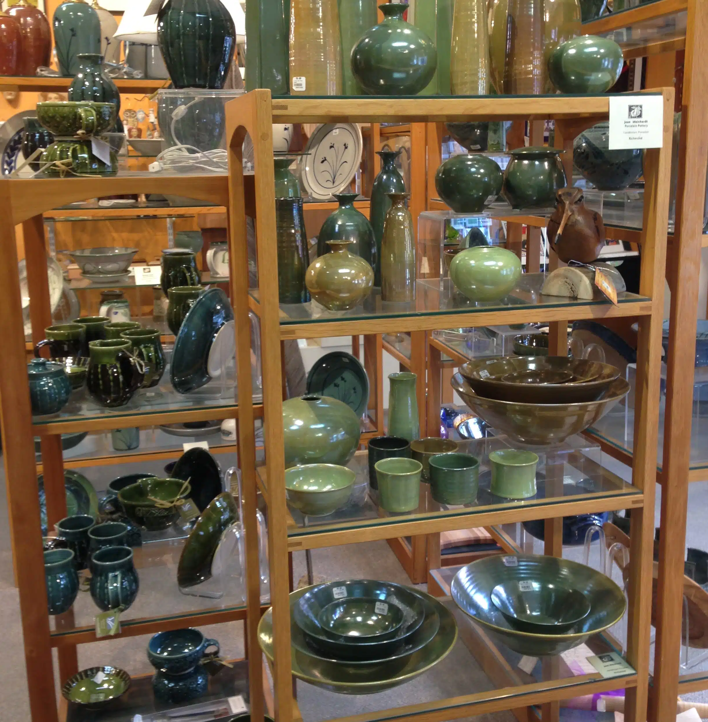 A display of various green and brown pottery items, including bowls, vases, cups, and plates, arranged on wooden shelves in a store.