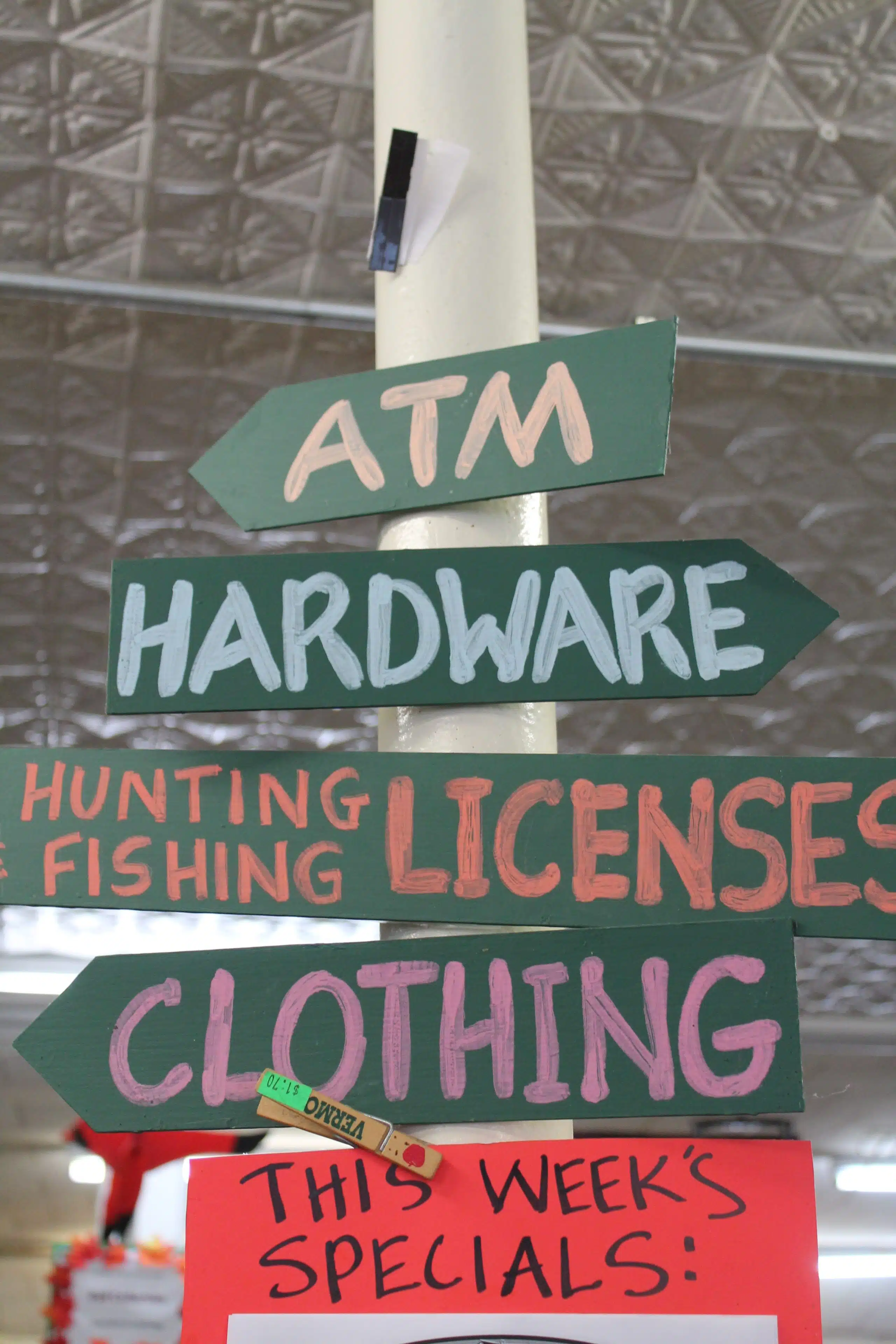 Directional sign with arrows pointing to ATM, hardware, hunting/fishing licenses, and clothing. A sign below reads "This Week's Specials.