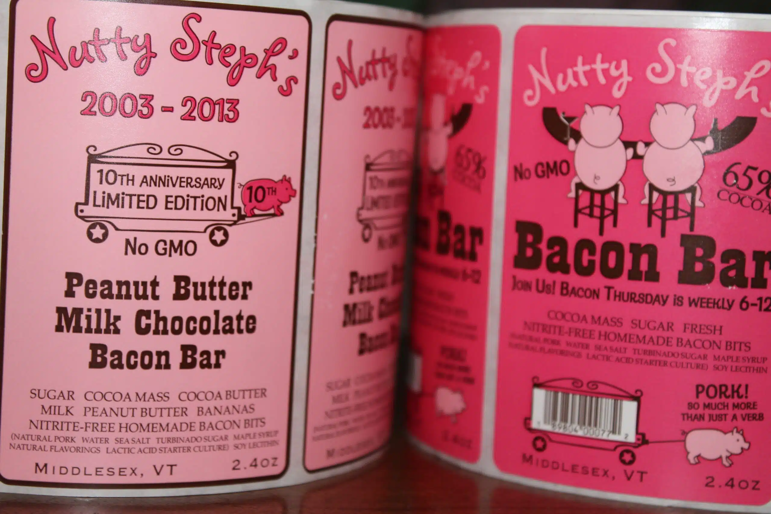 Close-up of two product labels for Nutty Steph's 10th Anniversary Limited Edition Peanut Butter Milk Chocolate Bacon Bar. Labels feature text details and an illustration of two pig heads.