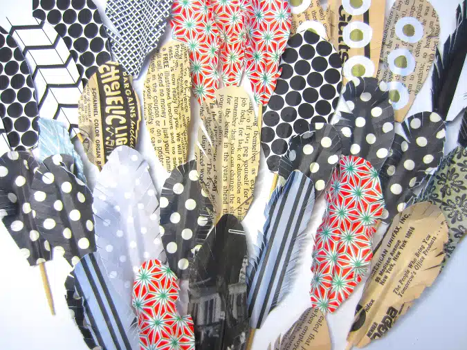 Assorted decorative feathers made from various patterned papers, including polka dots, text prints, stripes, and floral designs, arranged in a fan-like spread.