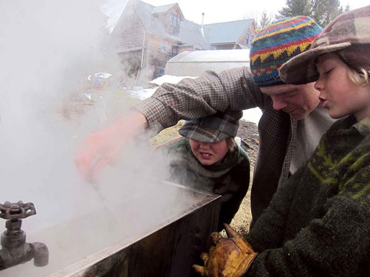 Fin, age 12, and Rye help their dad check the temperature of the steaming syrup in the evaporator.