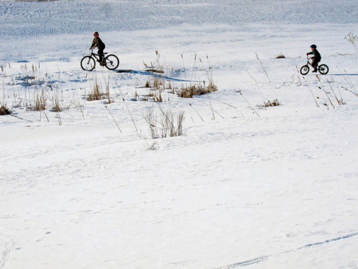 The boys pedal their bicycles across the last of the snow. 
