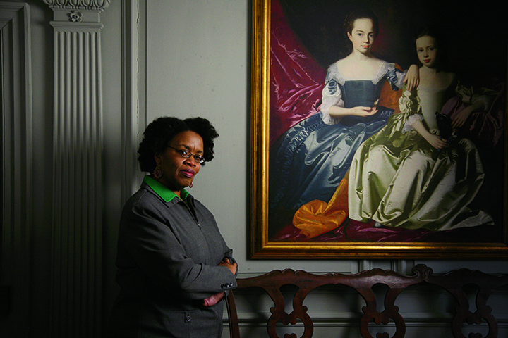 Olivia Searcy, education coordin­ator for the Royall House in Medford, Massa­chu­- setts, stands next to a repro­duction of John Singleton Copley’s portrait of Mary and Eliza­beth Royall.