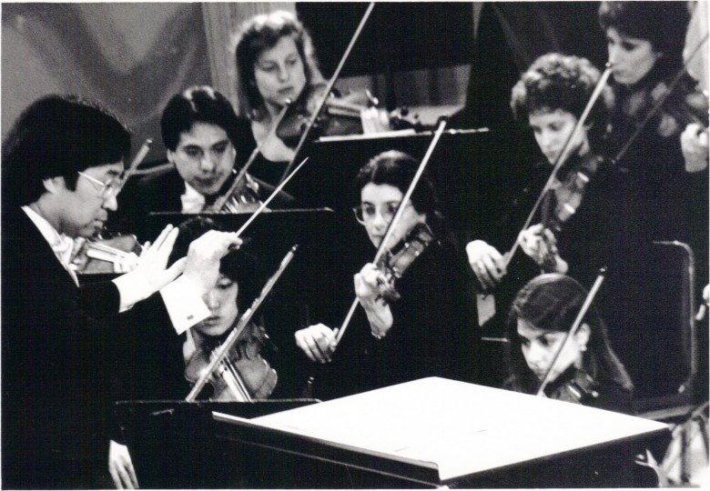 c. 1985: Conductor Toshi Shimada and PSO violinists in concert.