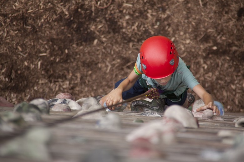 A young camper bravely ascends the rock wall. 