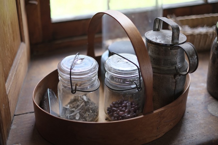 Detail of shaker carrying basket and jars of beans in the kitchen of the brick dwelling.