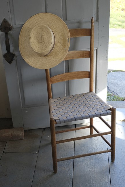 A handwoven chair and straw hat inside the garden shed.