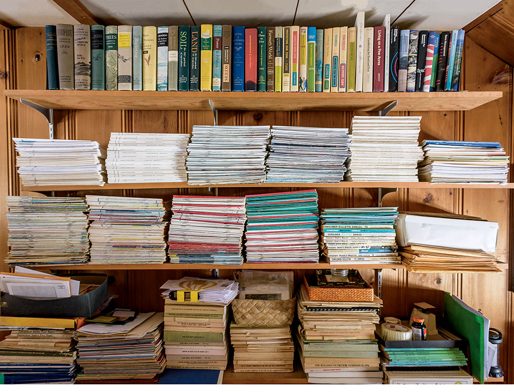 A wooden bookshelf filled with organized books, magazines, folders, and stacked papers in a home office.