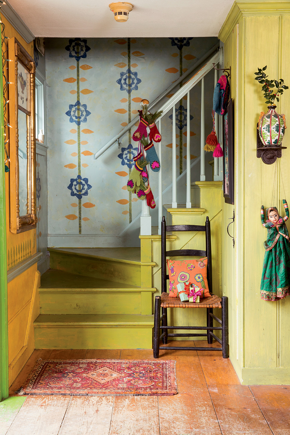 The stairway in Kristin Nicholas’s home is festooned with her art, from the hand-painted walls to the knitted mittens to the embroidered pillow.