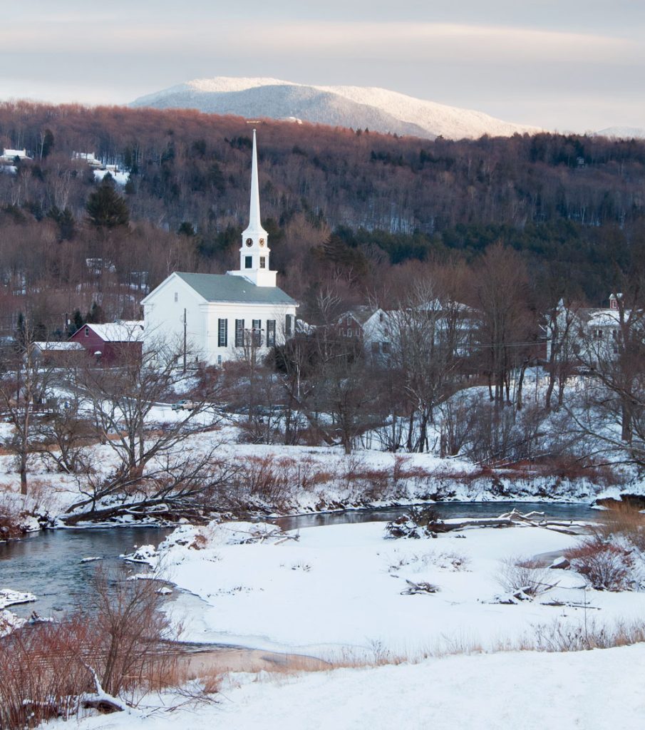 A serene winter landscape with a white church, snowy ground, and a mountain in the background.