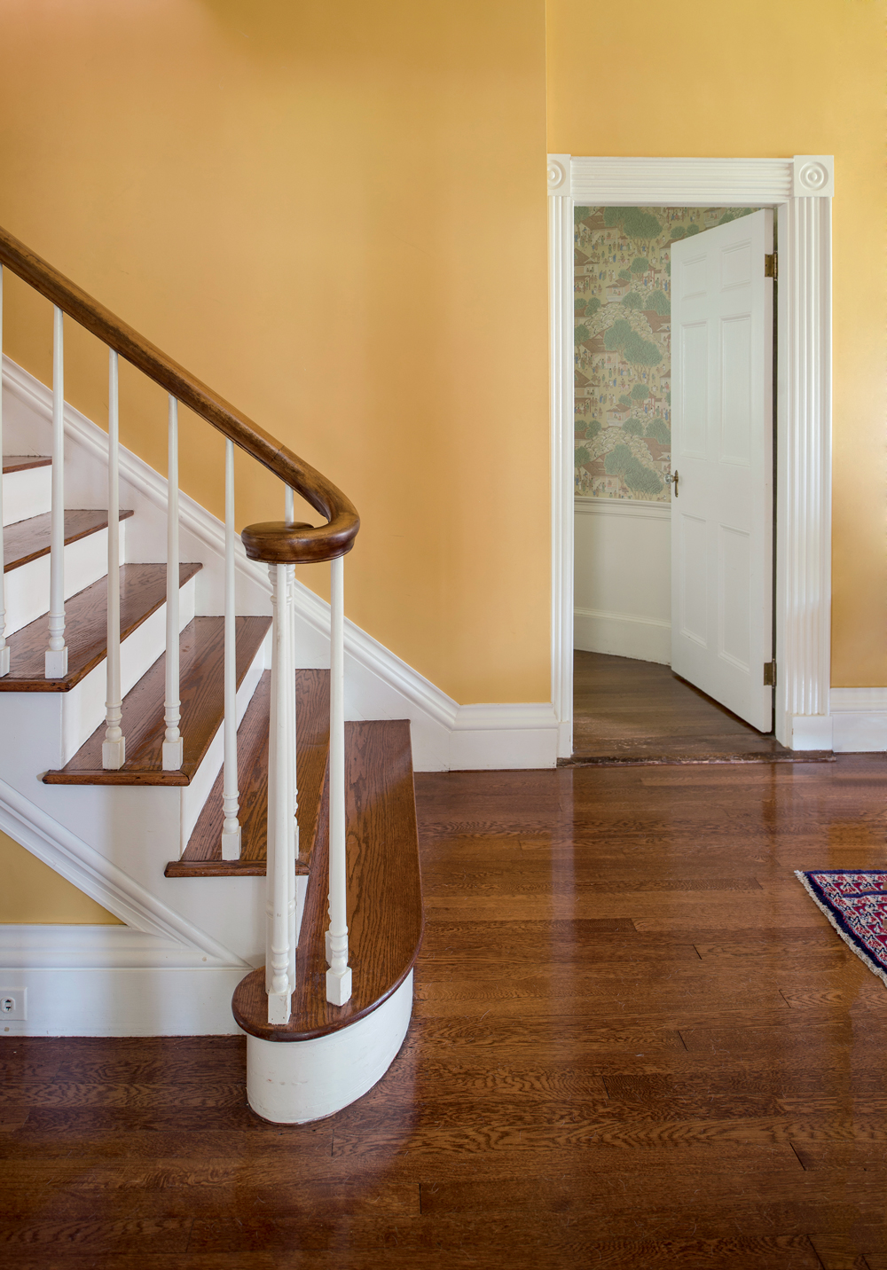 A hallway’s gleaming flooring and graceful staircase.