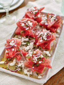 Watermelon salad with feta cheese, red onion, fresh mint, and a drizzle of olive oil on a white plate.