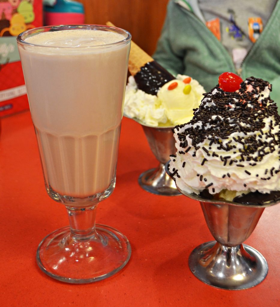 Milkshake in a tall glass next to two ice cream sundaes topped with whipped cream, sprinkles, and a cherry. One is the Friendly's Cone Head Sundae.
