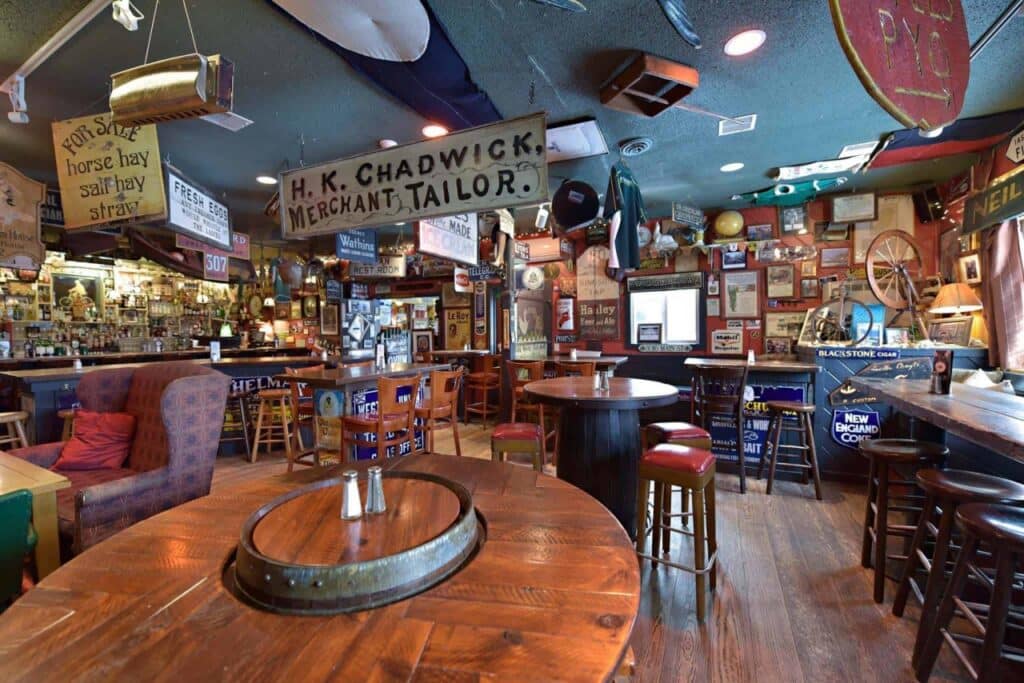 A cozy pub with wooden tables, bar stools, and vintage signs and memorabilia covering the walls and ceiling.