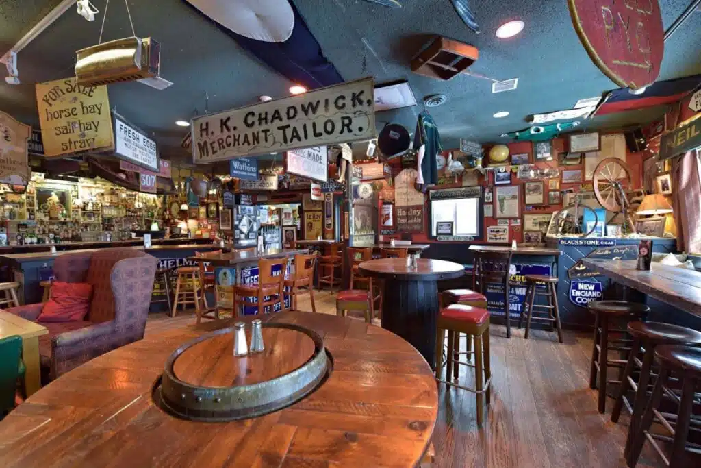 A cozy pub with wooden tables, bar stools, and vintage signs and memorabilia covering the walls and ceiling.