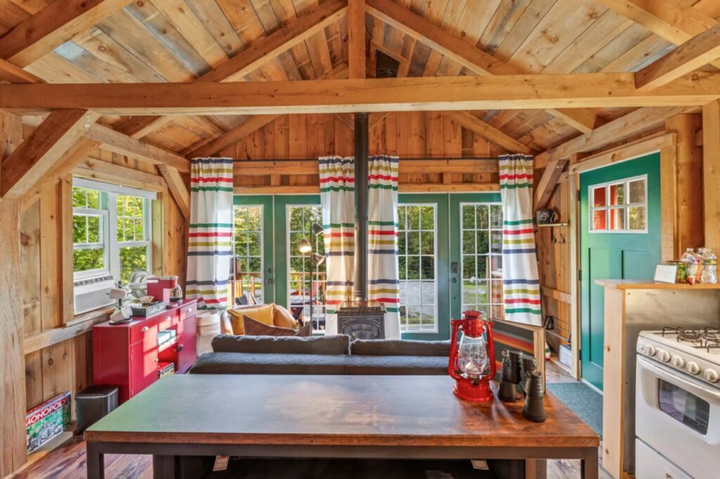 Cozy wooden cabin interior with striped curtains, red accents, and a large windowed door to the outside.