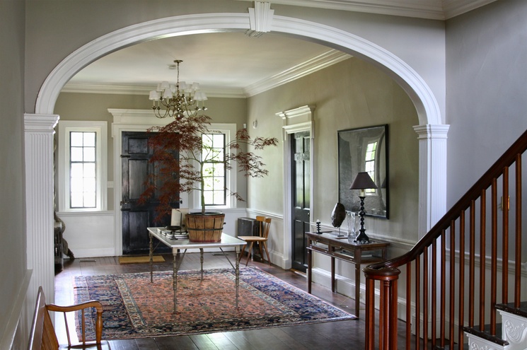 Bright entryway with an arched doorway, patterned rug, table with plant, and staircase on the right.