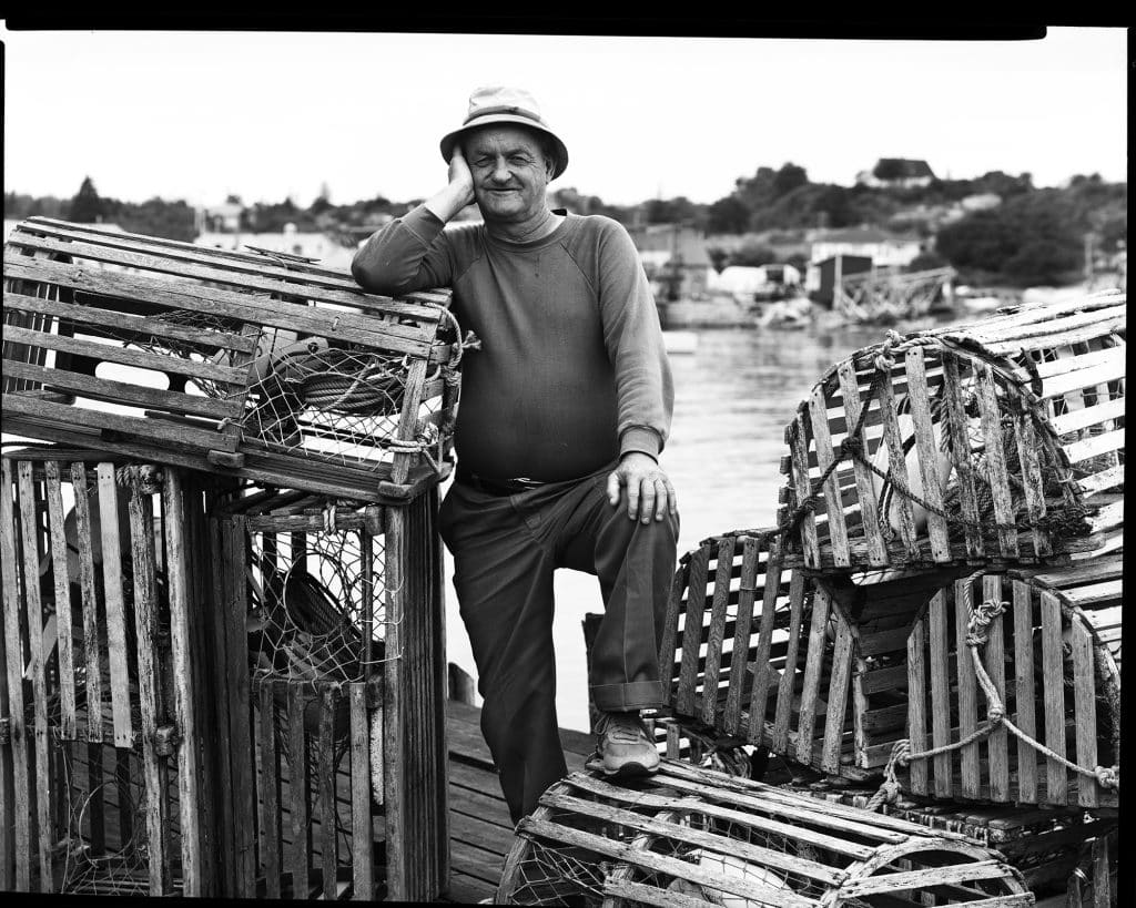 Man in a hat standing next to lobster traps on a pier.