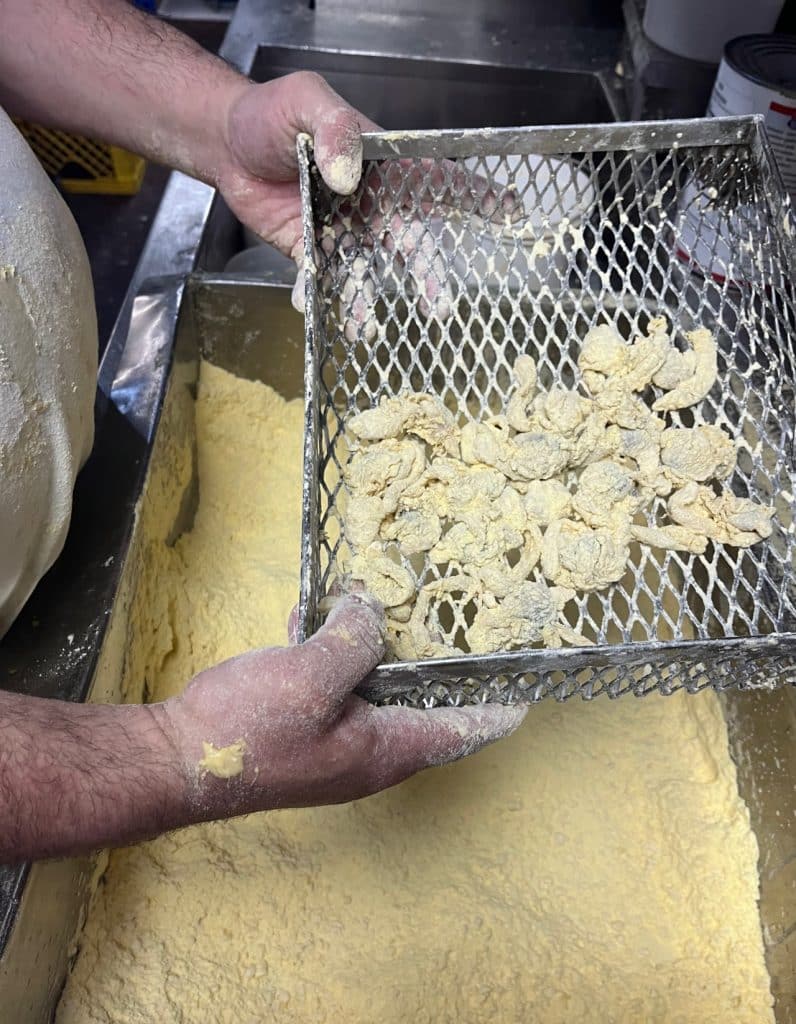 Person's hands holding a metal grate with corn flour battered clams at Woodman’s of Essex,